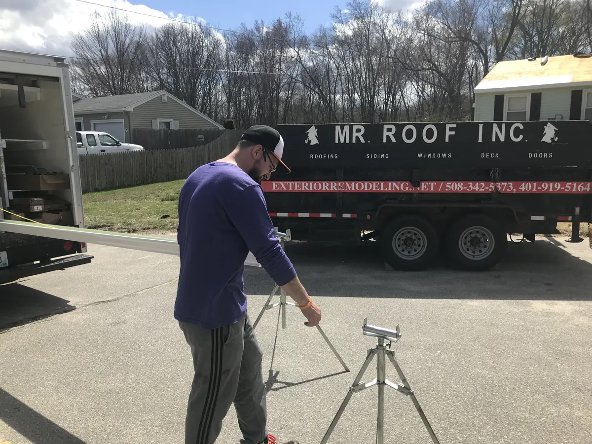 Mister Roof crew member preparing seamless gutter material beside a branded trailer
